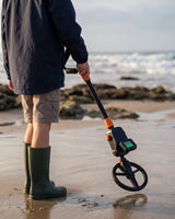 Détecteur de métaux enfant Ordetect tenu par un enfant vu de dos sur une plage française, bobine au-dessus du sable